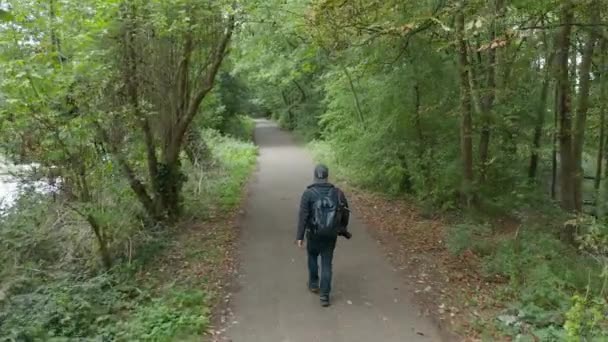 4k Vista aérea do homem com sua câmera andando ao longo de um caminho cercado por árvores — Vídeo de Stock