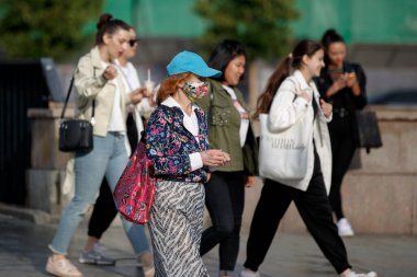 Moskova, Rusya, 21 Temmuz 2020: Mavi beyzbol şapkası takan ve çiçek desenli bir kumaştan yapılmış koruyucu maske takan bir kadın. Şehir merkezindeki caddelerde trafik yoğun.