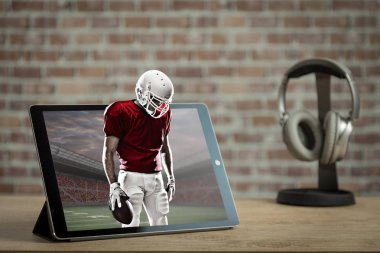 Kırmızı bir üniforma oyun oynama ve bir tablet dışarı geliyor futbol oyuncusu. Talep kavramı üzerinde bir futbol maçı izliyor.