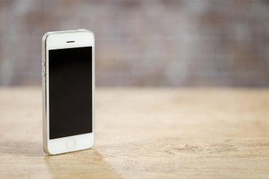 Bir tuğla duvar önünde ahşap bir masa üzerinde duran smartphone. Kopyalama alanı