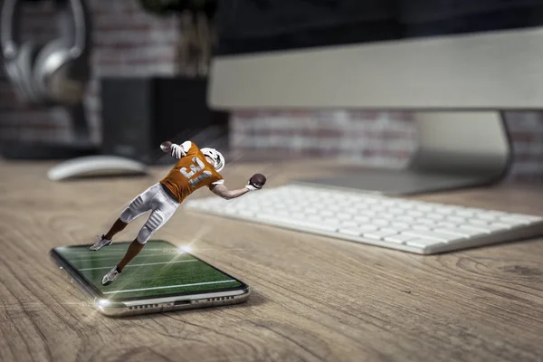 Football Player with a orange uniform playing and coming out of a full screen phone on a wooden table. Watching a football game on demand concept. copy space.
