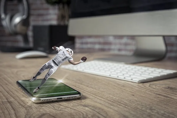 Football Player with a white uniform playing and coming out of a full screen phone on a wooden table. Watching a football game on demand concept. copy space.