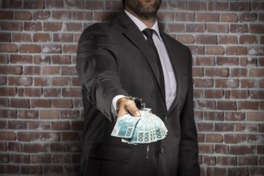 Brezilyalı adam para bir kelepçe ile faturalar bir hapiste tutan. yolsuzluk, yozlaşmış siyasetçiler, yasadışı işletmeler kavramı. tuğla arka plan.