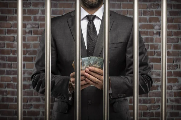 Brazilian man holding bills of money with a handcuff in a jail. concept of corruption, corrupt politicians, illegal businesses. brick background.