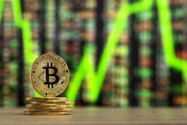 bir sayı grafiği önünde ahşap bir masada duran fiziksel bitcoin