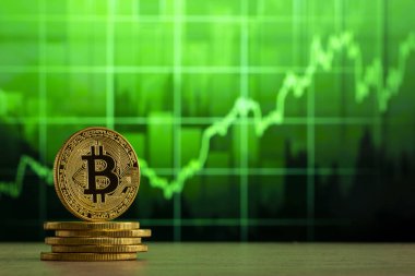fiziksel bitcoin Yeşil grafik önünde ahşap bir masada duruyor. Bitcoin Bull Market konsepti.