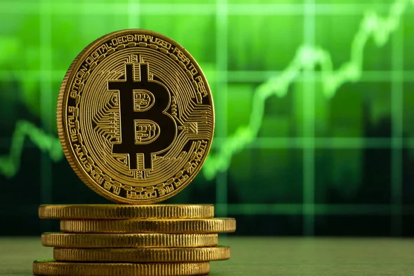 fiziksel bitcoin Yeşil grafik önünde ahşap bir masada duruyor. Bitcoin Bull Market konsepti.