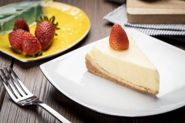 Tahta bir masada beyaz bir tabakta çilekli cheesecake.