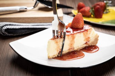 Tahta bir masada beyaz bir tabakta çilekli cheesecake.