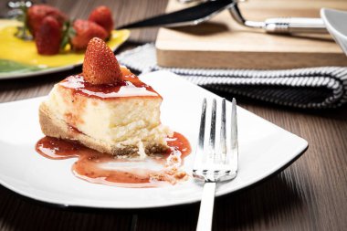 Tahta bir masada beyaz bir tabakta çilekli cheesecake.