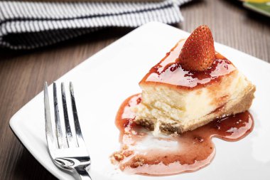 Tahta bir masada beyaz bir tabakta çilekli cheesecake.