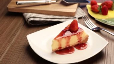 Tahta bir masada beyaz bir tabakta çilekli cheesecake. 4k