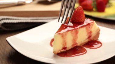 Tahta bir masada beyaz bir tabakta çilekli cheesecake. 4k