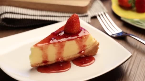 一片美味的草莓芝士蛋糕放在木制桌子上的白盘上 — 图库视频影像