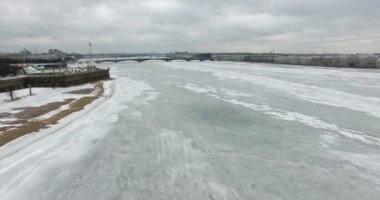 Havadan görünüm. Kışın bulutlu soğuk havalarda Neva nehri boyunca uçmak. Alacakaranlıkta Petersburg nehri üzerinde köprü. Donmuş nehir üzerinde uçuş kuşların yüksekliği.