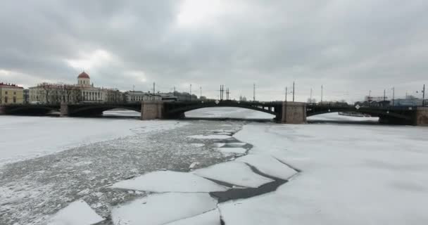 Légifelvétel. Repülés a Neva folyó mentén télen borús hideg időben. Híd a Petersburg folyón. A befagyasztott folyami repülők magassága. — Stock videók