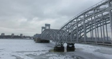 Havadan görünüm. Kışın bulutlu soğuk havalarda Neva nehri boyunca uçmak. Petersburg nehri üzerindeki köprü. Donmuş nehir üzerinde uçuş kuşların yüksekliği.