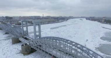 Havadan görünüm. Kışın bulutlu soğuk havalarda Neva nehri boyunca uçmak. Petersburg nehri üzerindeki köprü. Donmuş nehir üzerinde uçuş kuşların yüksekliği.