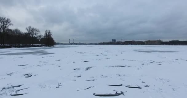 Вид с воздуха. Летит вдоль реки Невы в зимнюю пасмурную холодную погоду. Мост через реку Петербург. Высота птичьего полета над замерзшей рекой . — стоковое видео