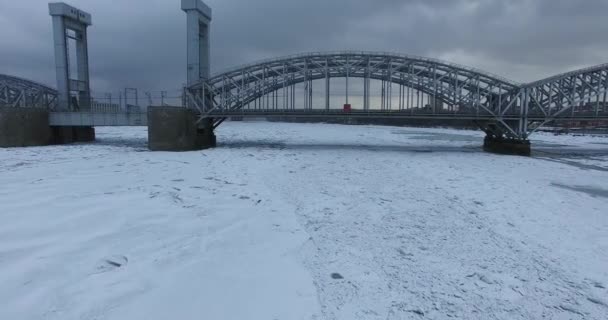 Luchtfoto. Vliegen langs de rivier de Neva in de winter overgegoten koud weer. Brug over de rivier de Petersburg. De hoogte van de vogelvlucht boven de bevroren rivier. — Stockvideo