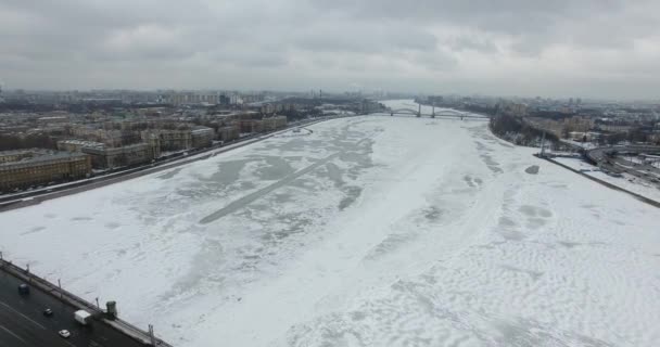 Havadan görünüm. Kışın bulutlu soğuk havalarda Neva nehri boyunca uçmak. Petersburg nehri üzerindeki köprü. Donmuş nehir üzerinde uçuş kuşların yüksekliği. — Stok video