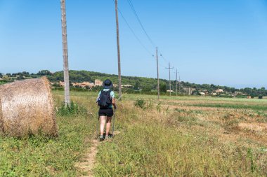 Girona, Katalonya, İspanya 'da çember saman balyalarıyla tarlalar arasında yürüyen bir kadın yürüyüşçü..