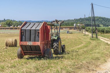 Bir çiftliğin yanında saman balyası olan bir traktör..