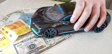 Rishon lezion, İsrail - 2 Mart 2019: kağıt para dolar servet hryvnia gibi çeşitli ülkelerin üzerinde ön tekerlekler ile onun parmak siyah Bugatti Chiron metal oyuncak ayakta tutan erkek