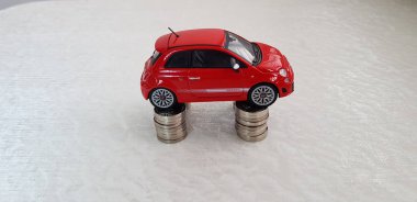 Rishon lezion, Israel - march 2, 2019: small red fiat 500 abarth toy stands on four stacks of one israeli shekel coins arranged one on another in columns clipart