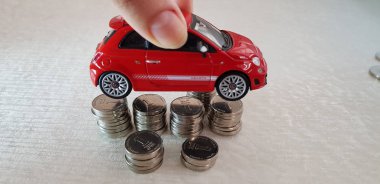 Rishon lezion, İsrail - 2 Mart 2019: küçük kırmızı fiat 500 oyuncak İsrail Şekeli sikke yığını üzerinde onun elinde bir başka sütunlar üzerine düzenlenmiş bir kız tutar