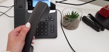 Beyaz oje giyen kadın siyah cep telefonu yere yakın bir zımba ve beyaz masada küçük yeşil etli bitki ofis telefon sol elinde tutan