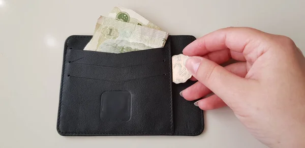 black wallet with one yuan banknote in it while female hand takes out two hong kong dollars coin