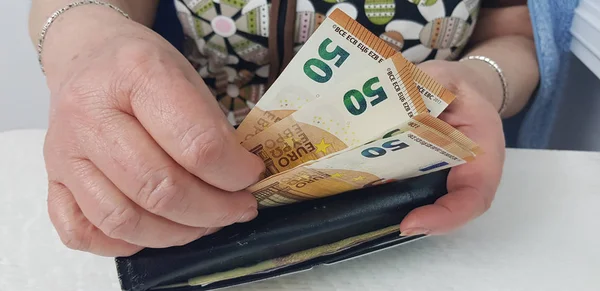 elderly woman holds in hands euro cash money putting it into black old wallet