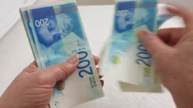 200 şekel banknotlar sayma kıdemli kadın ve beyaz masaya koyar
