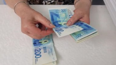 beyaz masa üzerinde şekel banknotlar sayma kıdemli kadın