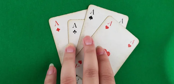 girl holds fingers on four playing cards aces of all suits on green background