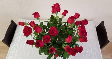 Büyük bir buket kırmızı güller iki boş sandalyeyle beyaz masada duruyor.