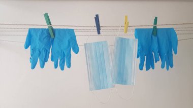 Çamaşır ipine asılı iki yüz koruma maskesi ve dört lastik eldiven çamaşır makinesinden sonra kuruması için.