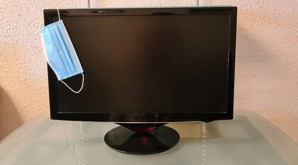 surgical face protection mask hanging on a black computer monitor with blank screen