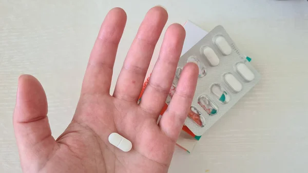 white pill on a palm over open box with more pills on white table