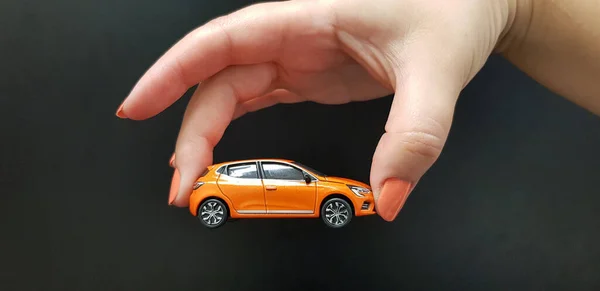 Metalen Oranje Auto Speelgoed Vrouwelijke Hand Geïsoleerd Tegen Zwarte Muur Rechtenvrije Stockafbeeldingen