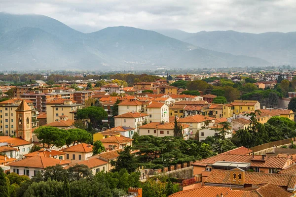 Pisa, Toskana/İtalya - 25.10.2018: Ünlü Eğik Kule'den Pisa'nın panoramik manzarası. İtalyan yaşam evleri, kafeler, kiliseler, sokaklar. Ufukta dağlar var. Bulutlu gökyüzü.