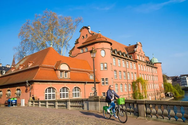 Strazburg, Alsace/Fransa - 06.04.2019: Saint-Thomas Devlet İlköğretim Okulu, Saint-Martin köprüsü, bisikletli yaşlı kadın, yürüyen insanlar