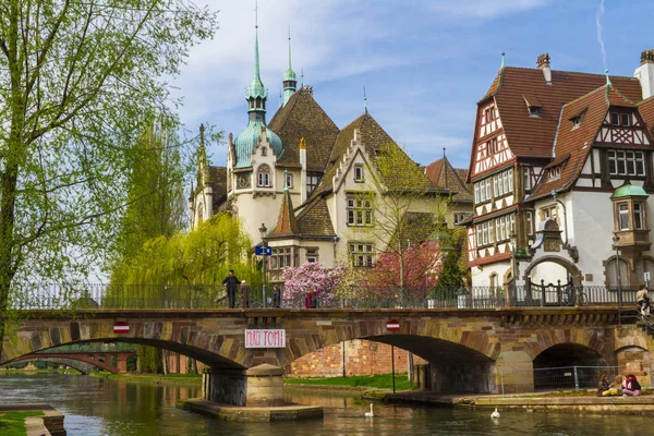 Strazburg, Alsace/Fransa - 01.04.2019: Ill nehri kıyısında lisenin inşası. Söğüt, kiraz ve elma ağaçları, eski kemer köprü, yarı ahşap bina ile Bahçe. Parlak güneşli bir gün