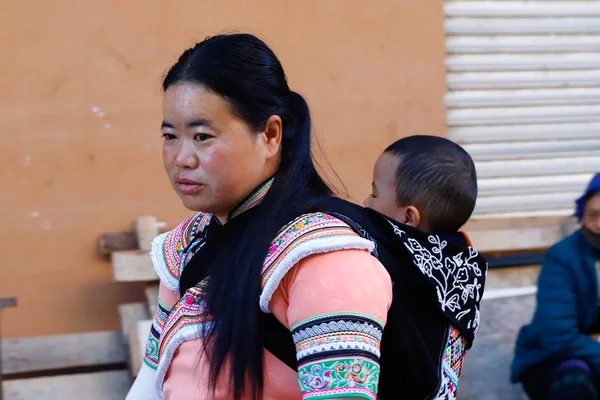 Uma mulher com um bebê em roupas típicas em uma aldeia no sul de Yunnan, China — Fotografia de Stock