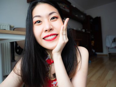 Evde oturan ve sevinçle, mutlu yüz kameraya bakarak heyecanlı Asya Çin genç kadın portresi. Çok güzel bayan arkadaş görmek çok güzel, yapma video aile Internet, Merhaba, merhaba deyin