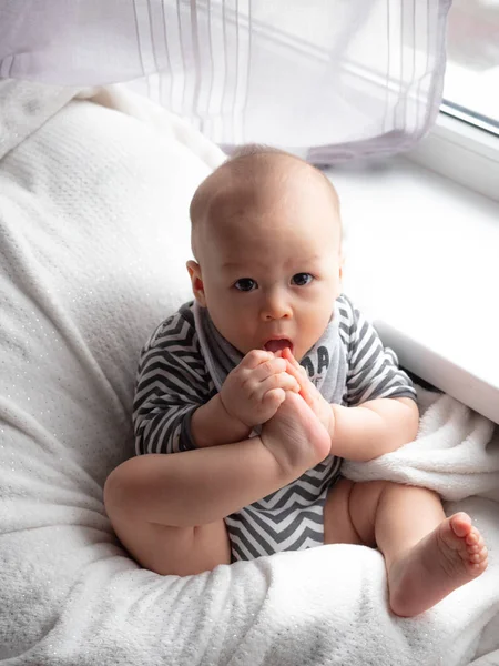 Close up ritratto di carino bambino ragazzo sdraiato su una coperta succhiare le dita dei piedi, piedi, piede, misto metà razza est asiatico caucasico ragazzo guardando felice la fotocamera . — Foto Stock