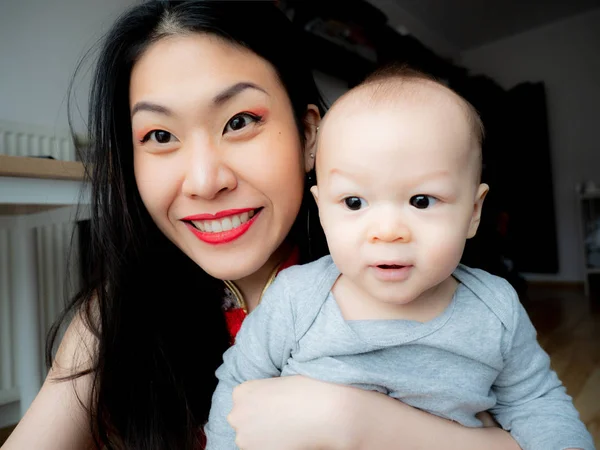 A portrait of excited Asian Chinese mother and son sitting at home and looking at camera with joy, happy face. Adorable lady glad to see friend, family making video call by Internet, say hello, hi