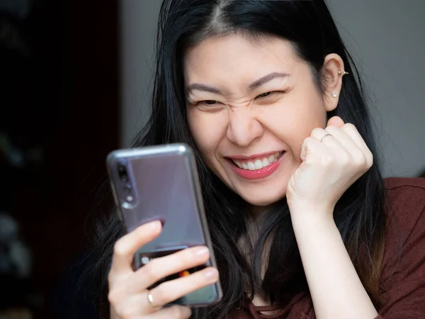 Son derece heyecanlı genç Asyalı güzel kadın tarafından mobil app satış mesaj smartphone, holding, cep cep telefonu sevinçle çığlık seyir euphoric kız kazanan bakarak hayran. Büyük gözleri