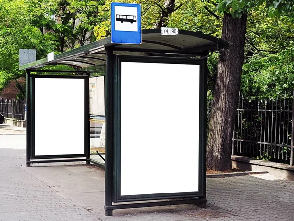 Straßenbahnhaltestelle, Wartehalle, weißer, leerer Platz für Straßenanzeigen, Werbetafel, Attrappe, Attrappe, Beschilderung, Bushaltestelle. vertikale weiße Plakatwand an der Bushaltestelle in der Stadtstraße. im Hintergrund Park. — Stockfoto